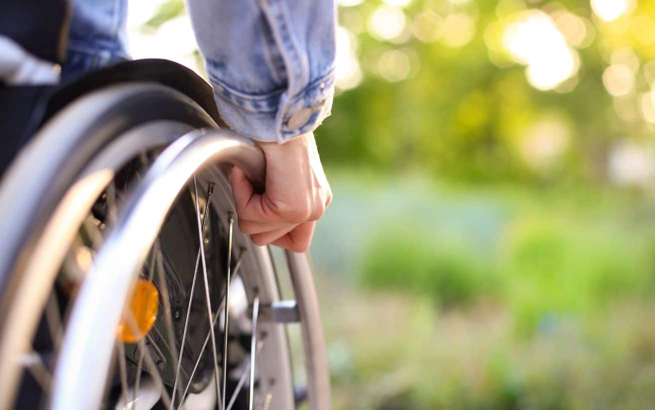 Close-up of a hand on a wheelchair wheel, with a blurred green background.