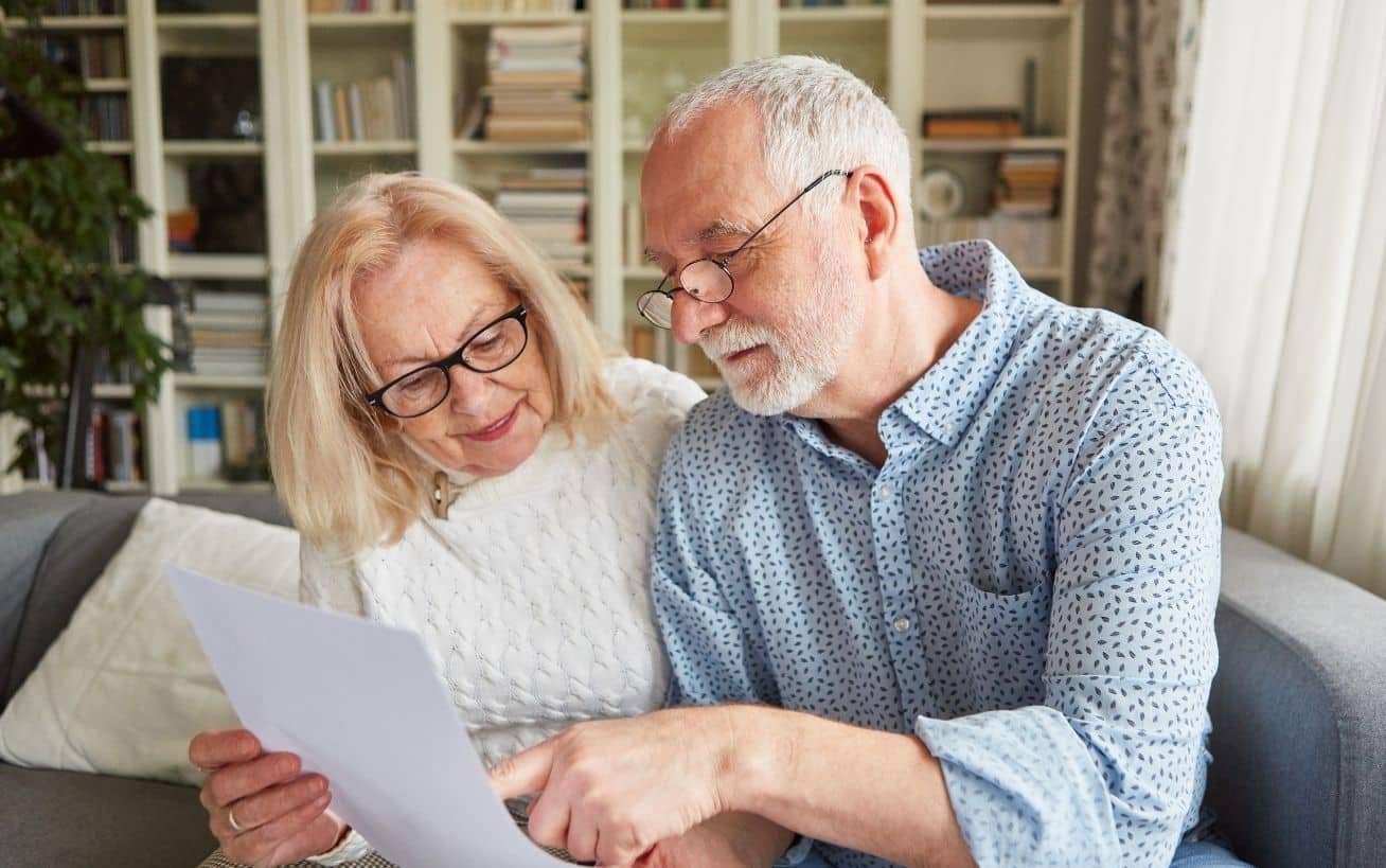 Elderly couple reading a document together on a sofa in a cozy living room.