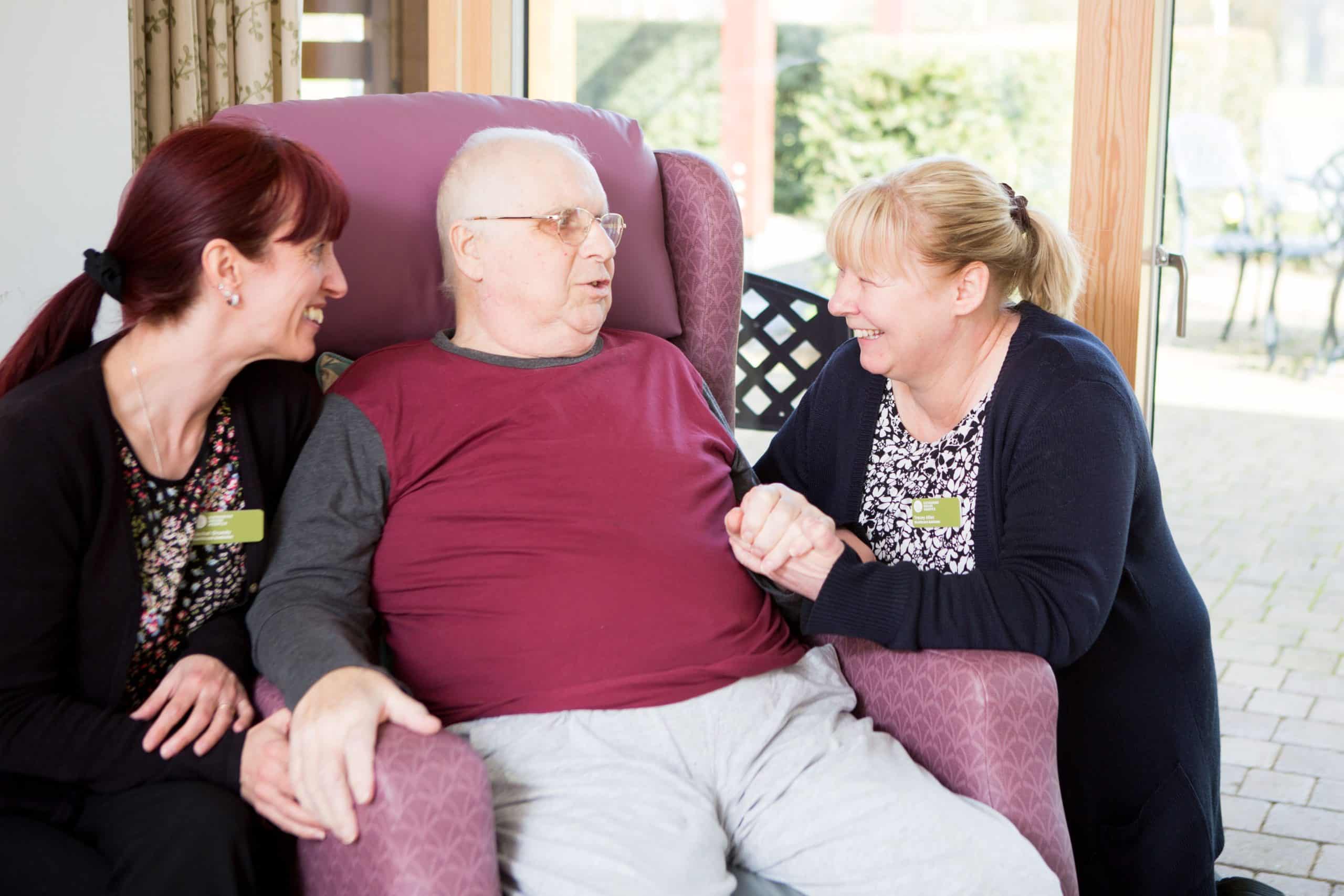 Man sitting with two women smiling and holding his hands.