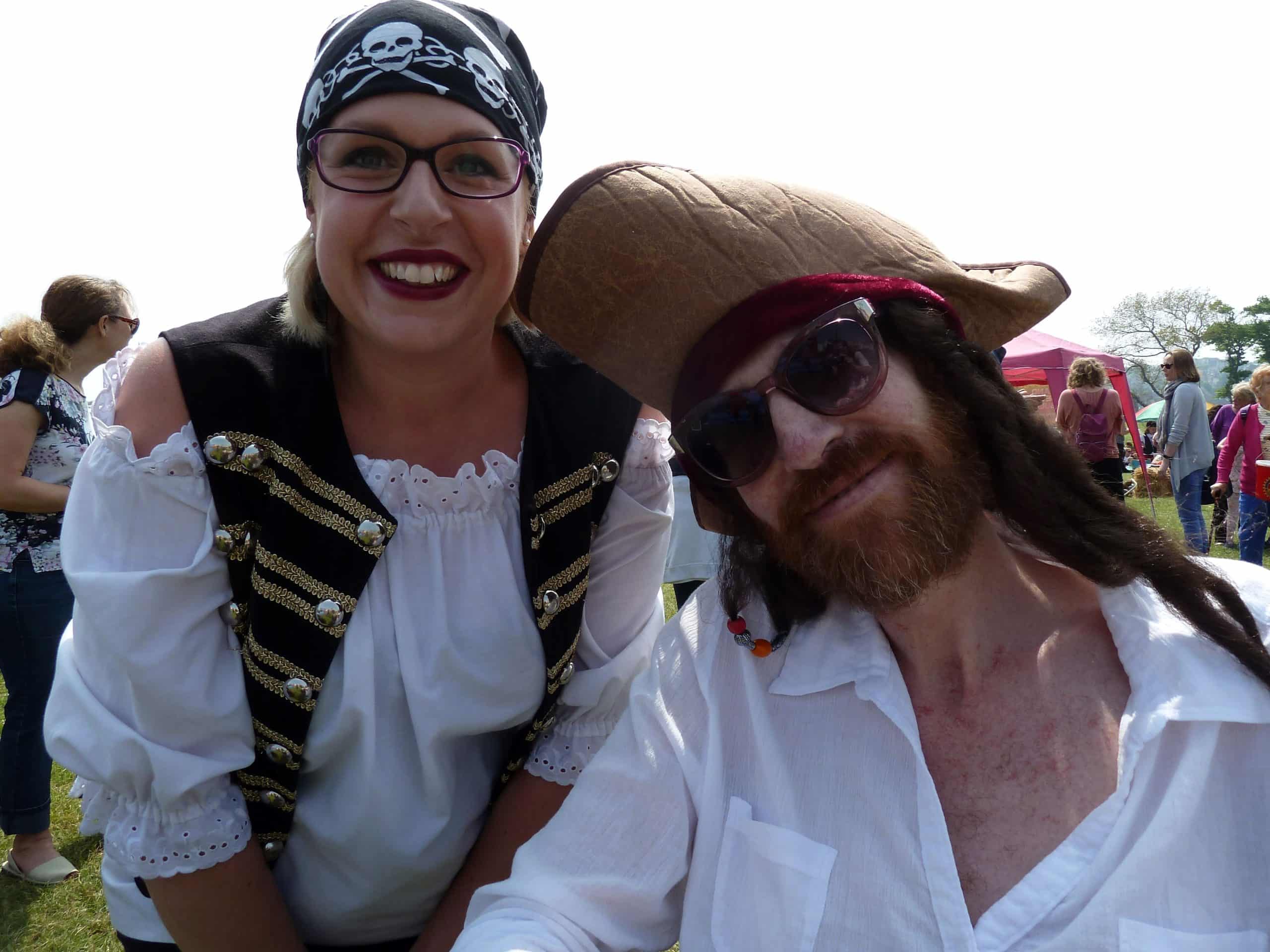 Two people dressed as pirates smiling at an outdoor event.