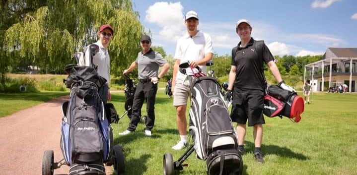 Employee fundraising and match fundraising Four people with golf bags stand on a golf course, smiling under a sunny sky.