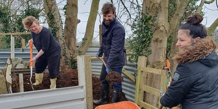 Firstsource and Lloyds garden volunteers Three people are working together, shoveling soil in a garden area surrounded by trees.