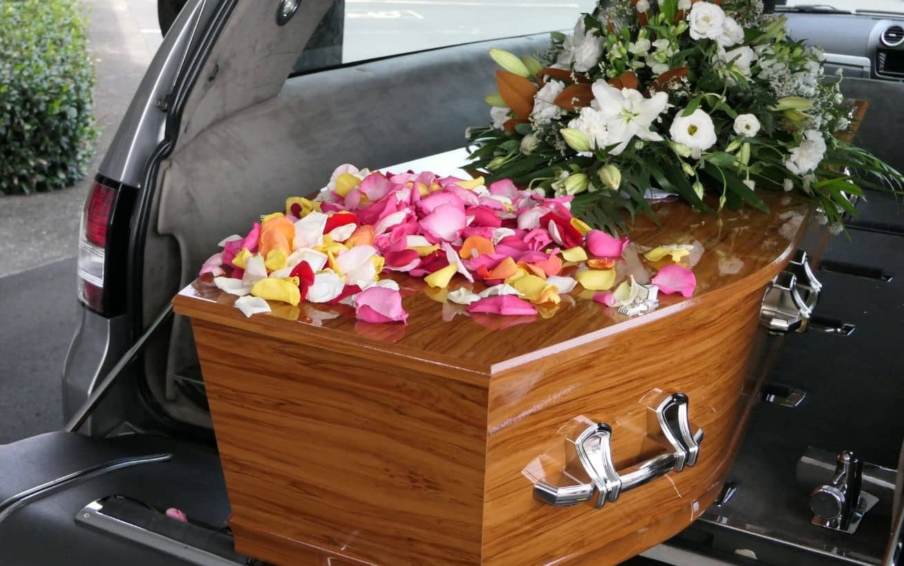 Wooden coffin with colorful rose petals and a floral arrangement inside a vehicle.