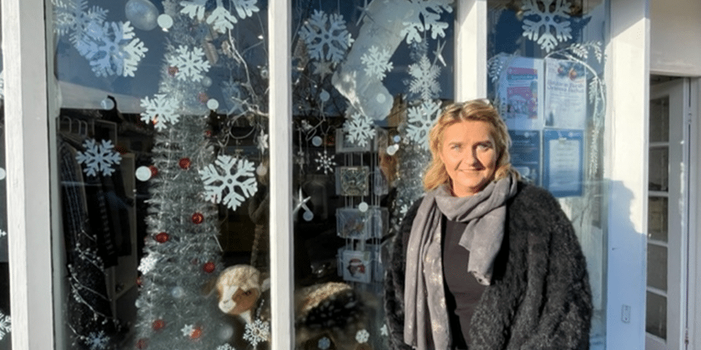 Woman standing in front of a festive window with snowflake decorations and a silver tree.
