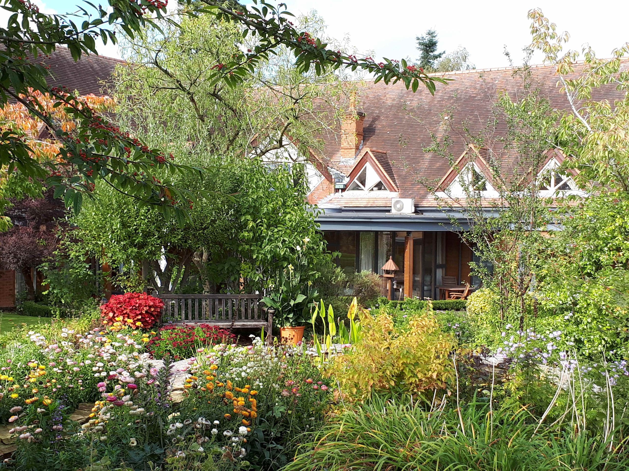 A lush garden with colourful flowers and trees in front of Katharine House Hospice.