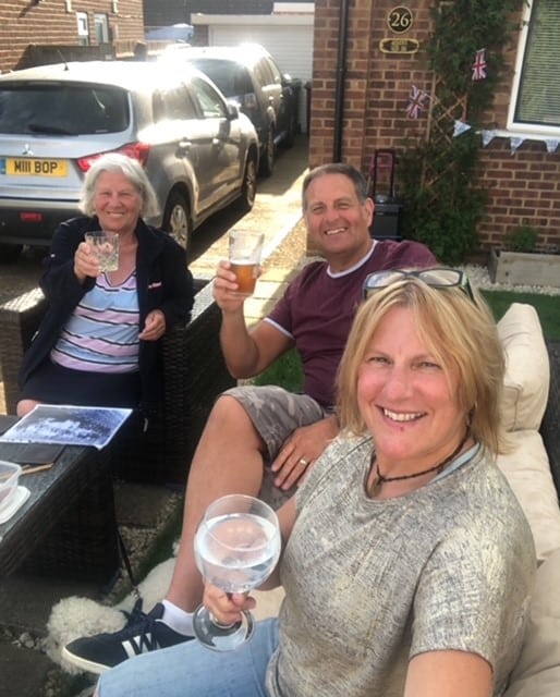 SHIRLE~3 Three people sitting outside on a patio, smiling and holding drinks for a selfie.
