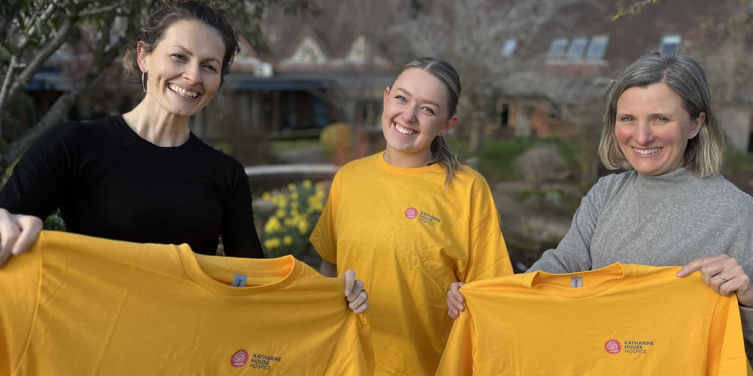 T shirts cropped Three women smiling and holding yellow T-shirts outdoors.