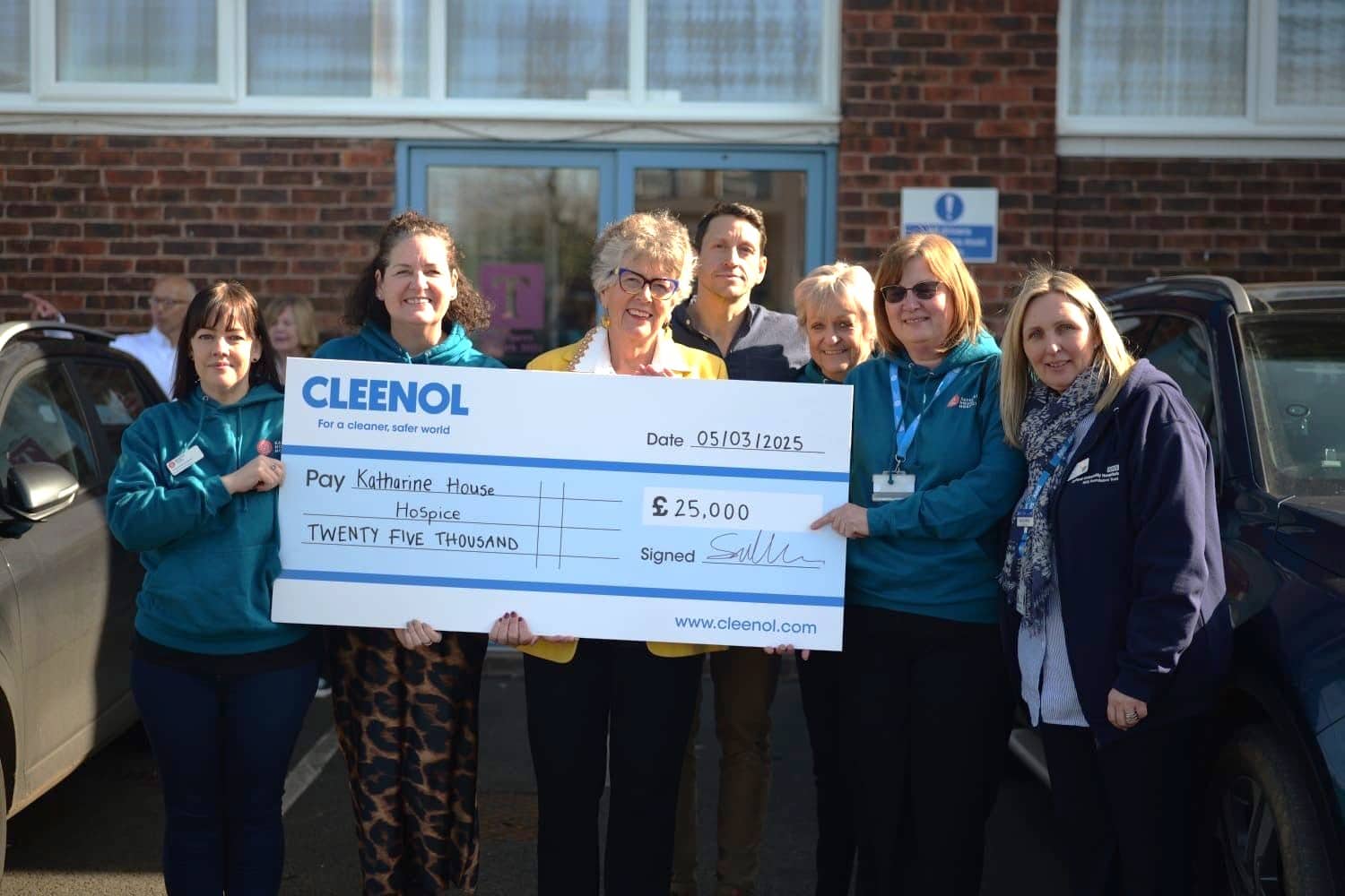 Project 75 chq presentation A group of people standing outside holding a large presentation check for charity.