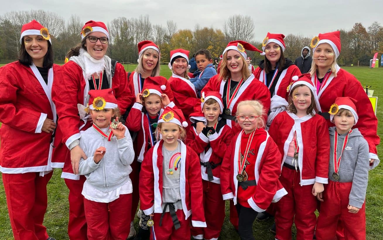 A group of children and adults dressed in Santa costumes and wearing medals pose together outdoors after completing the Katharine House Hospice Santa Fun Run.