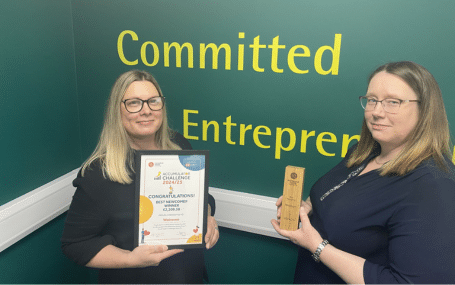 Walraven Best Newcomer banner Two women holding an award and a certificate in front of a wall with the words "Committed Entrepreneur."
