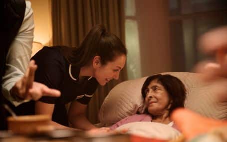 A caregiver smiles and talks to a woman resting in bed at a hospice.