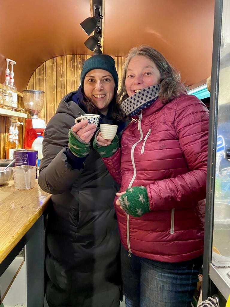 Nikki & Sarah at Brew Box on Tractor Run night Two women in winter coats smiling and holding cups inside a horsebox that has been converted into the cosy Brew Box coffee shop.