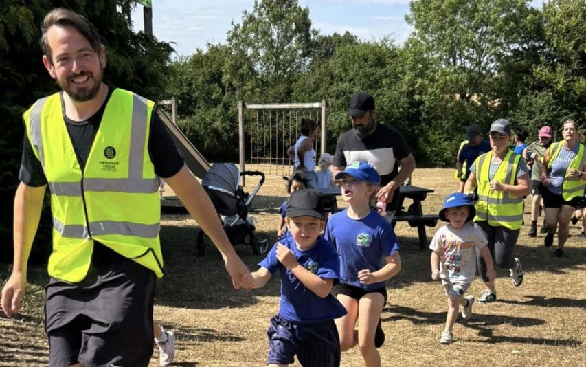 Chacombe School banner Adults and children, some in high-visibility vests, walk and run outdoors on a sunny day.