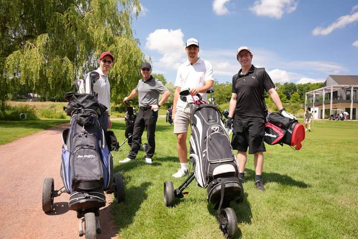 GRAF UK golf day Four people with golf bags stand on a sunny golf course, smiling for the camera.