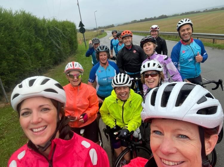 London to Paris day 3 A group of cyclists in helmets and bright jackets smiling on a road in northern France during the London to Paris cycle challenge for Katharine House Hospice.