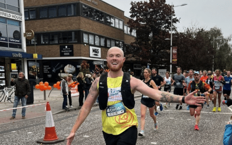 A smiling runner with arms outstretched and wearing a yellow Katharine House Hospice fundraiser's T-shirt during the Oxford Half Marathon.