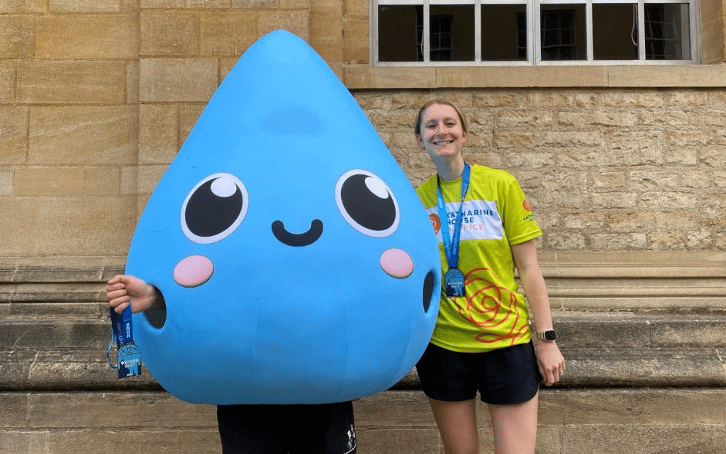 Person dressed as a large water droplet stands next to a woman wearing the Oxford half medal and wearing a yellow Katharine House Hospice T-shirt.