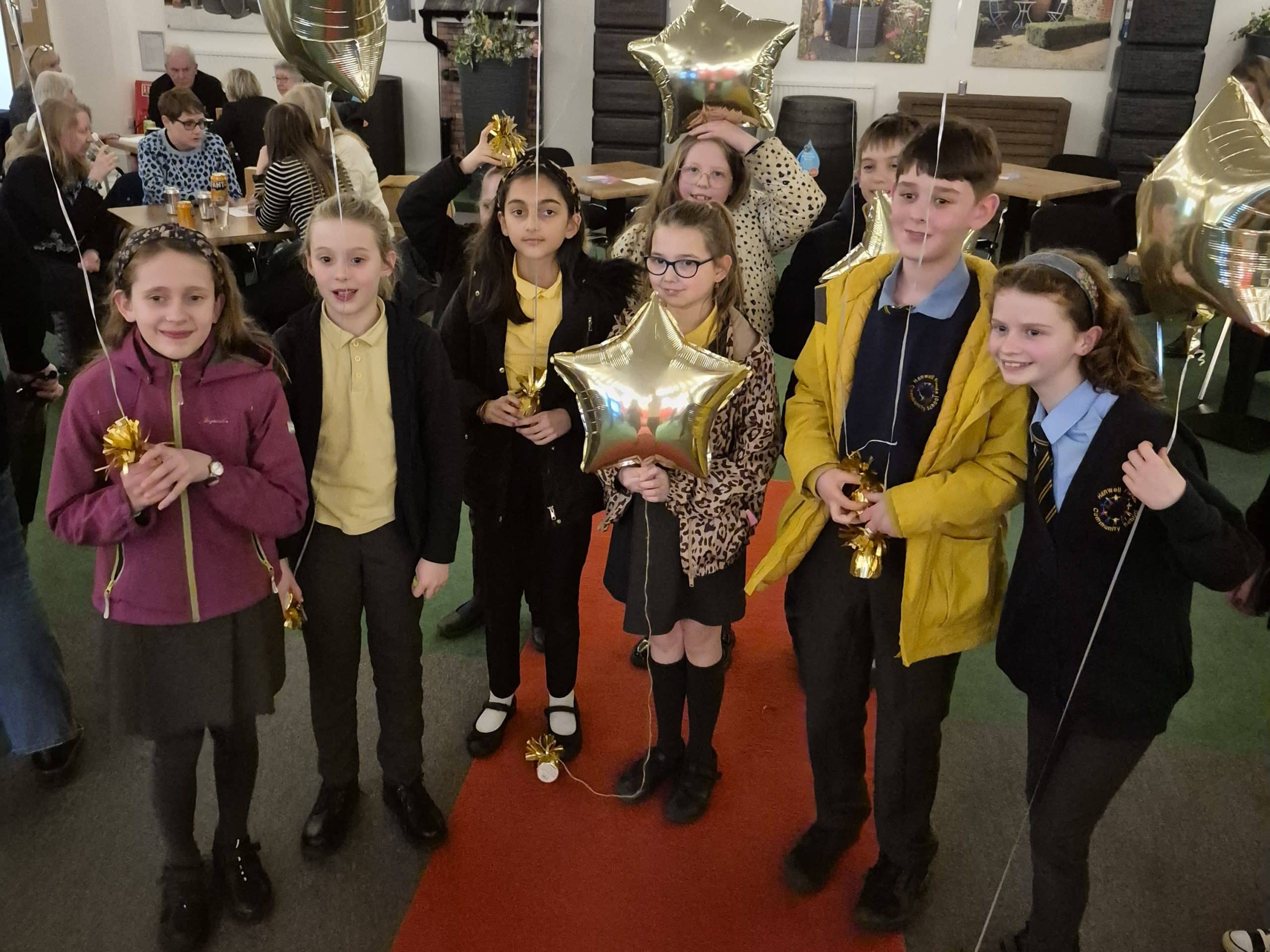 A group of children holding gold star balloons celebrating a win at the Katharine House Hospice Accumulator Challenge.